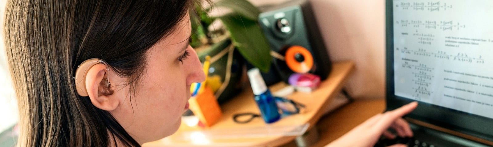 Teen girl with hearing aid attends class online. Photo by Sladic/Getty Images