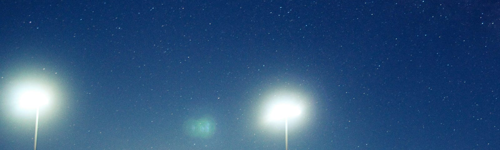 A lone player stands with his bat on his shoulder from deep in the outfield as other players warmup on the field.