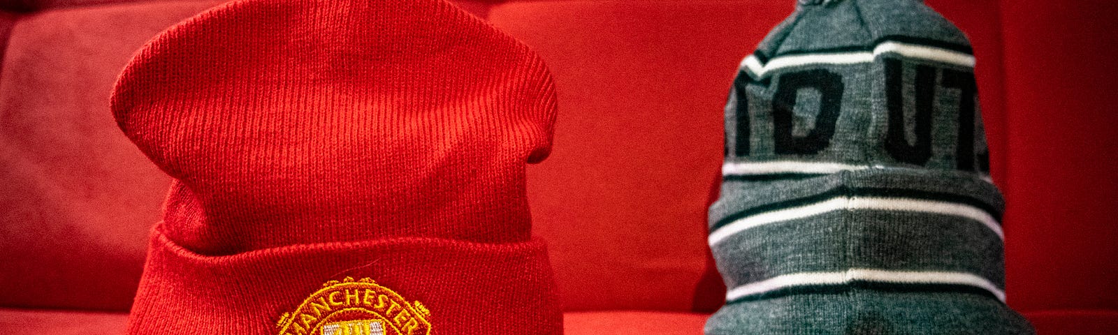 A red Manchester United beanie hat sits on a seat next to a grey Manchester United woolly hat