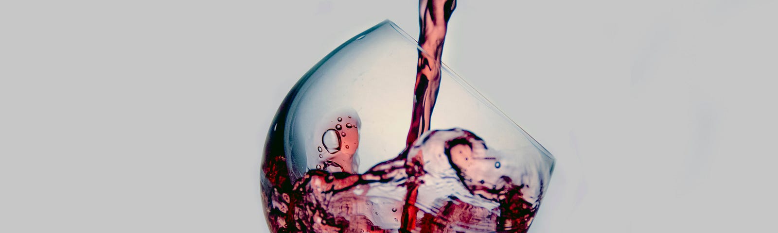 A tilted wine glass with wine being poured into it from out of the frame on a white background.