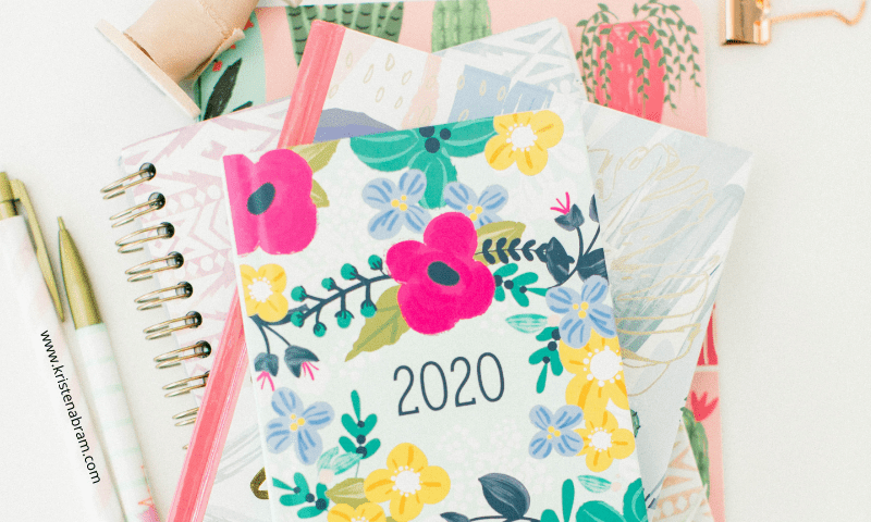 A stack of floral print journals, one with the numbers 2020 across the front cover, and two pens to journal with.