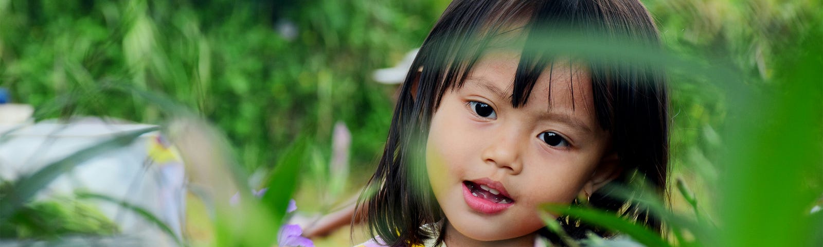 Young kid with dark hair and eyes plays, looking at someone hiding , perhaps.