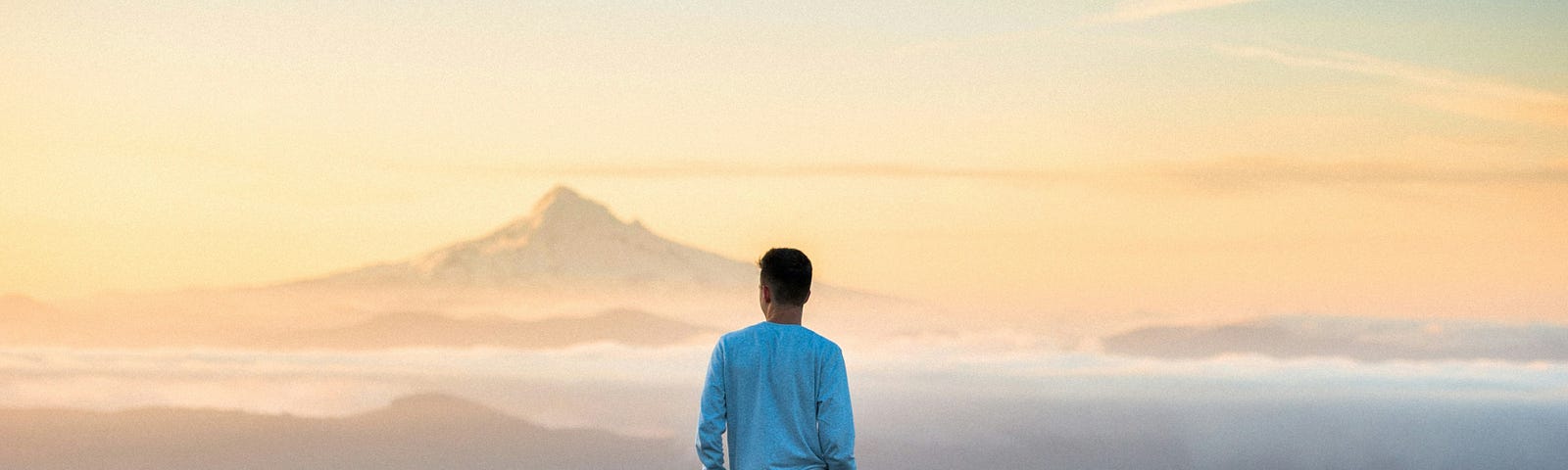 Man standing on a cliff and looking out deep in thought.