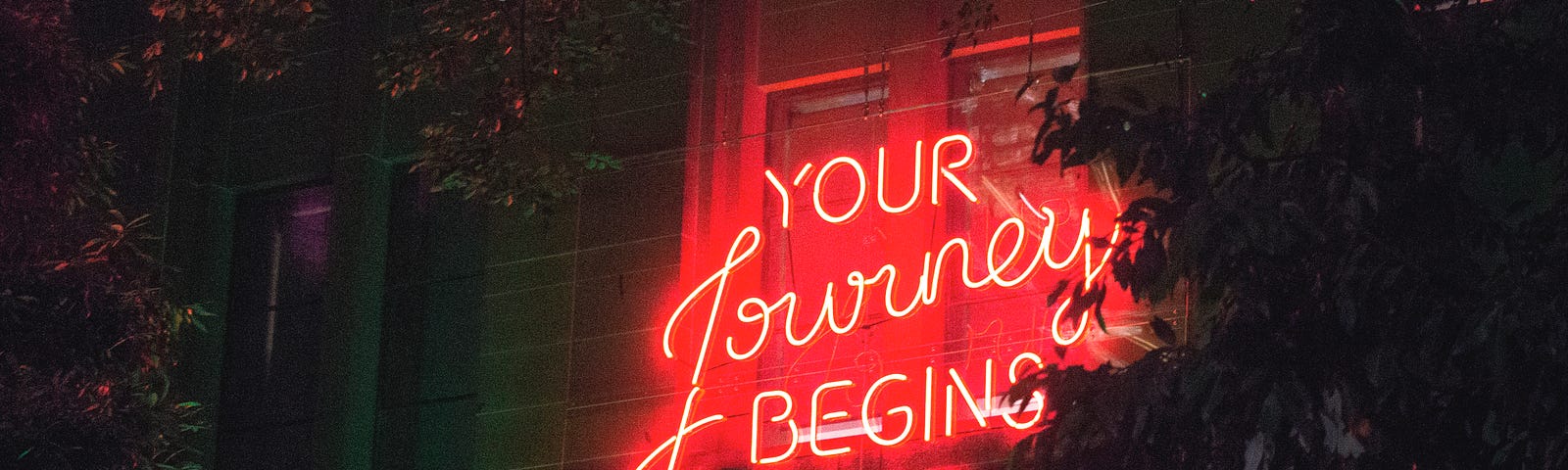 A red neon sign over a neon green entry that reads, “Your Journey BEGINS HERE”.
