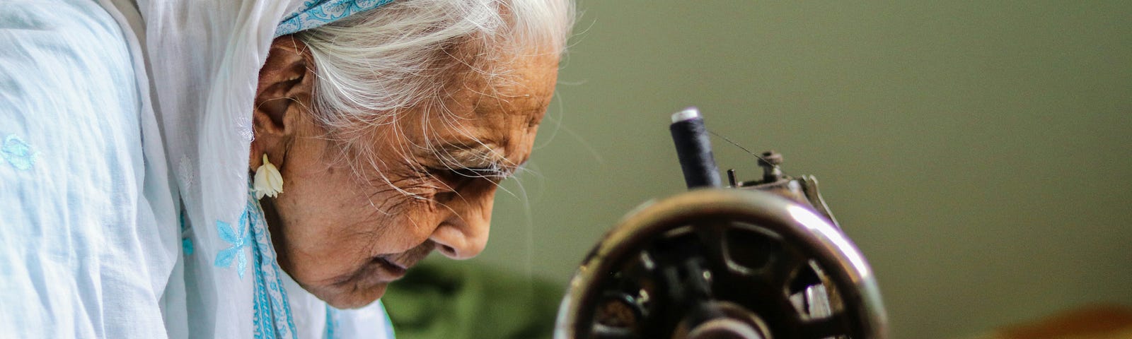 An older adult is straining to see the needle area on a hand-operated sewing machine.