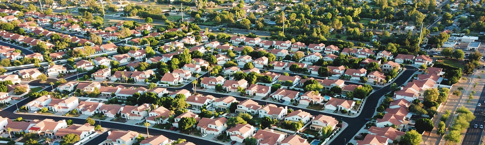 A bird’s-eye view of modern suburb. The houses have tiled roofs. There are multiple trees. Everything is tidy.