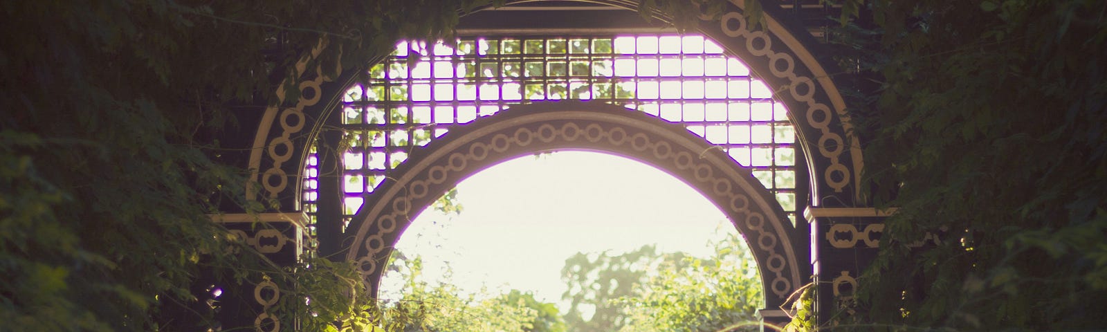 beautiful woman from the back walking in sunlight in a garden under an archway