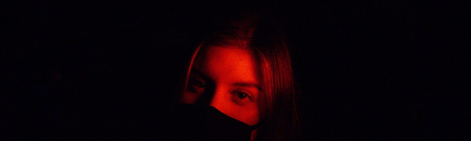 Young woman looks slightly to her right as she faces us. Her face is softly illuminated in an otherwise dark photo.