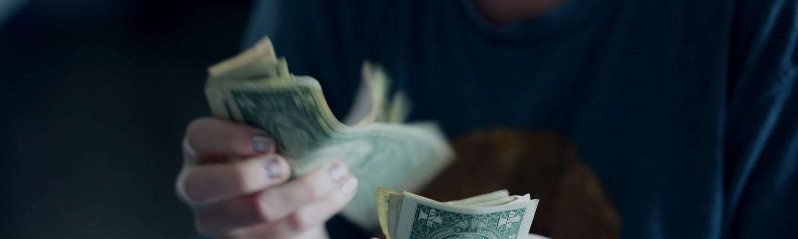 A person counting one dollar bills in their hands.