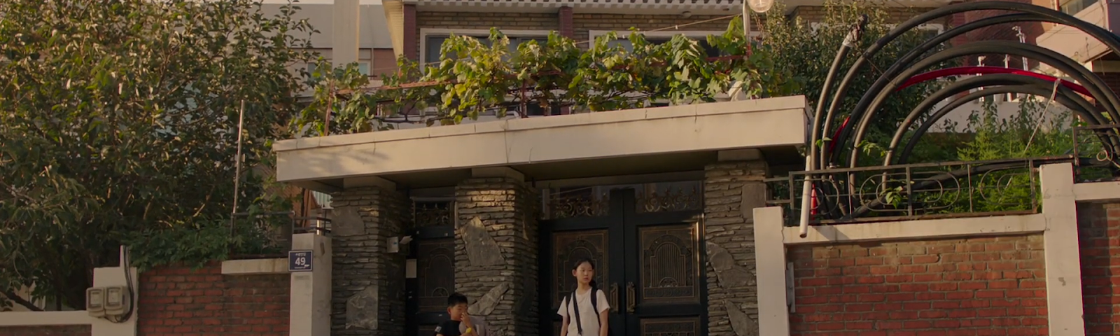 Film still from MOVING ON, of siblings Okju and Dongju in front of the house’s exterior, standing on the side of the road.