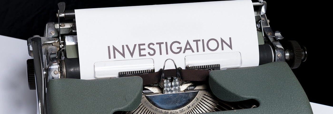 An antique typewriter with a piece of paper that reads, “Investigation.”
