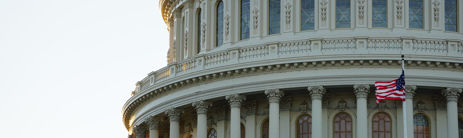 Closeup photo of the U.S. Capitol dome with an American flag foreground right.