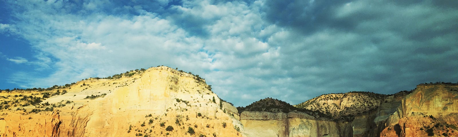 An escarpment above a meadow with billowing clouds drawing near.