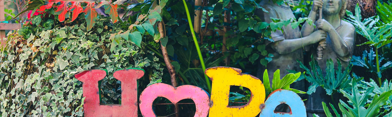 The word “hope” spelled out in colorful letters with a statue of two children in a forested background.