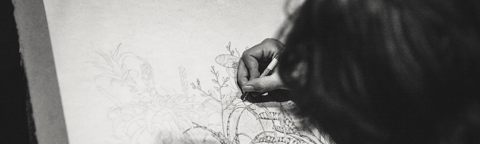 Person drawing artsy flowers on a piece of paper. The picture is in black and white because art