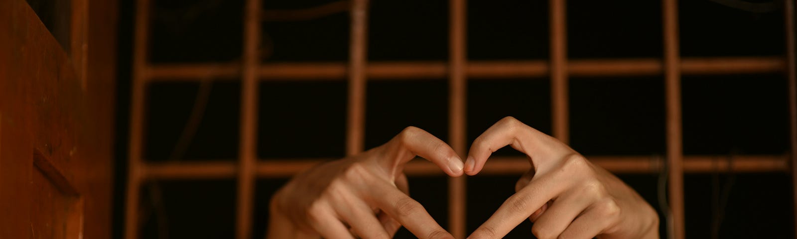 A person's hand coming out of jail's cell, making the gesture of a heart.