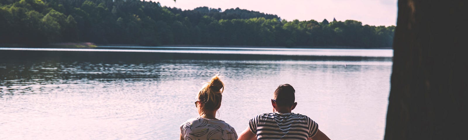 Couple sitting side by side by a lake.