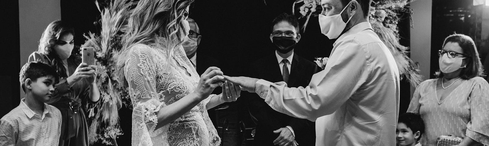 A woman slides the ring on a man’s finger while the family looks on.