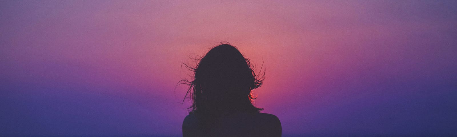 black silhouette showing woman looking out onto graduated red, blue, and purple sky