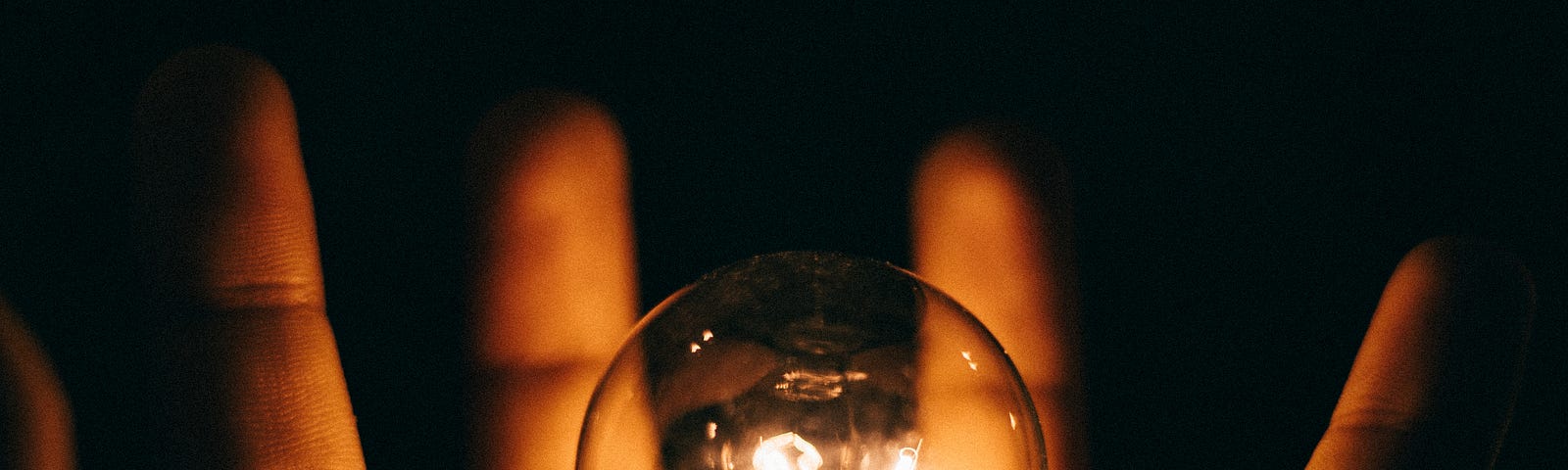 Open hand extends away from us, with a traditional round lightbulb (filament aglow) floating above it. Black background.