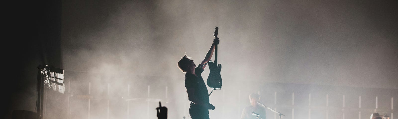 In a picture at a rock concert, a band member is holding up his guitar to the crowd