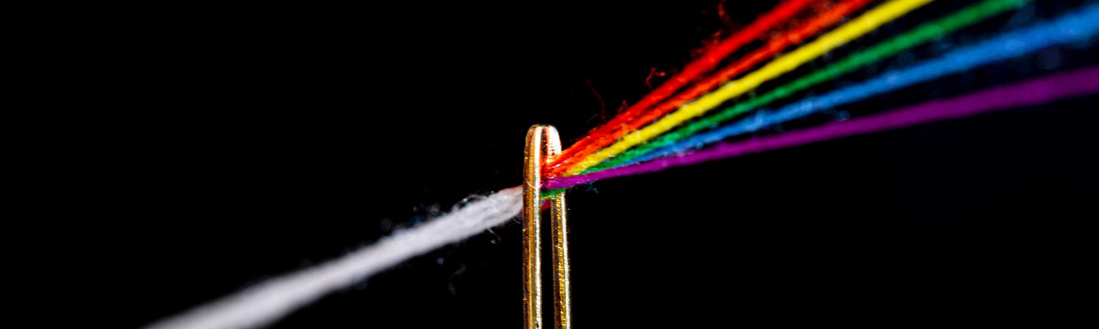 a white thread drawn through the eye of a needle turns into threads in all of the colors of the rainbow