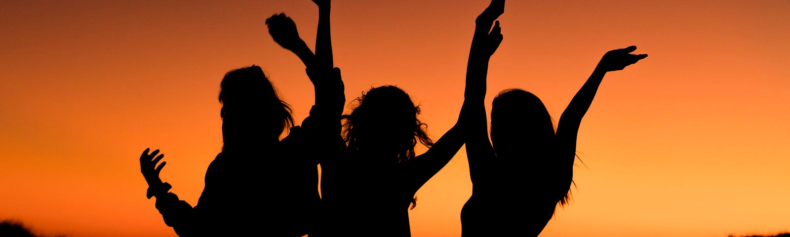 Three women dancing on an Ibiza beach at sunset