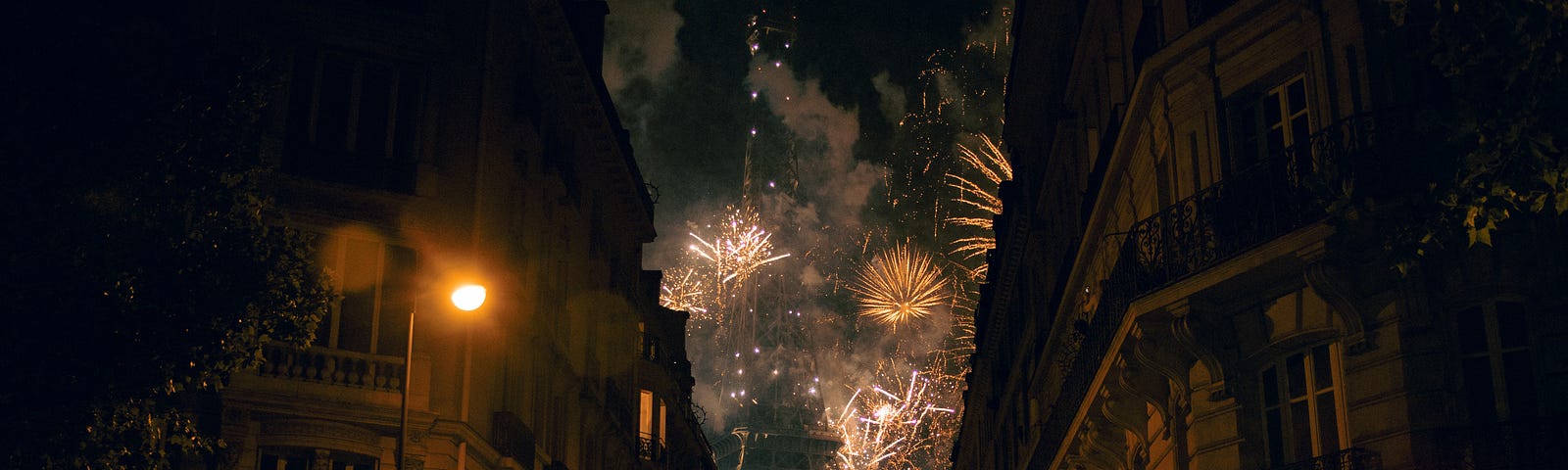 A firework at night time, viewing between two buildings to the Eiffel Tower.