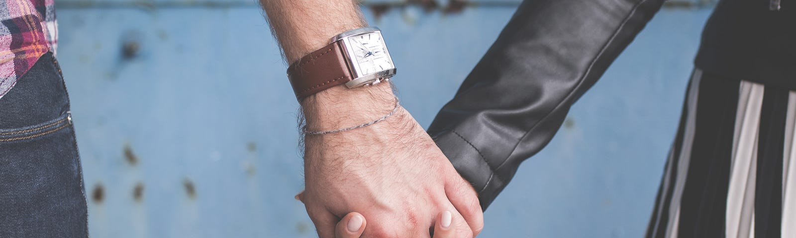 Two people holding hands. One person has a watch on and they are interlinking their fingers.