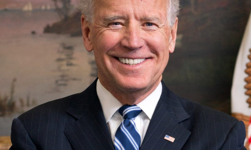 Official White House photo of Joe Biden. He is smiling, wearing a black suit and a blue and white striped tie.