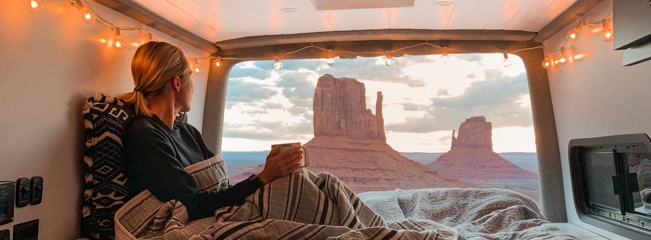 A woman in the back of a camper van overlooking the scenery.