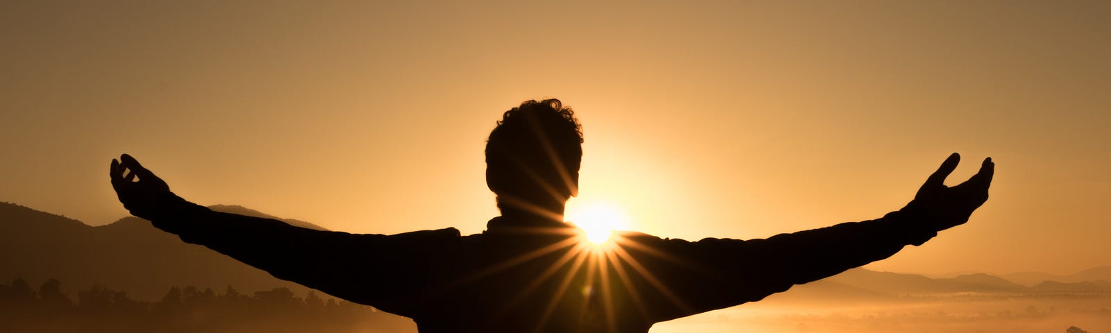 An image of a silhouette of a man standing with his arms spread, and in the background you see the sunset.