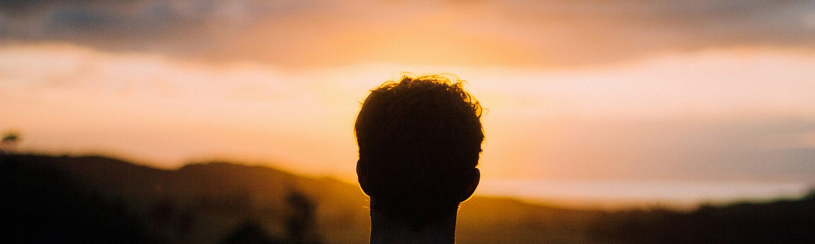 A person standing alone and facing the sun at dawn.