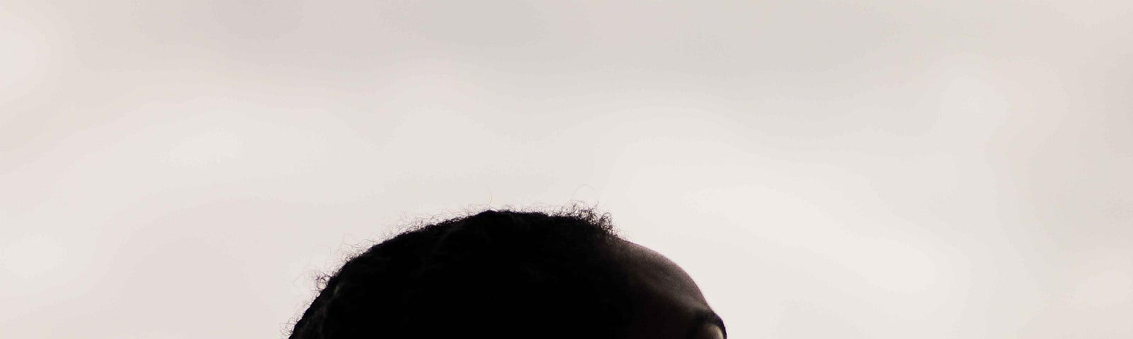 Black woman with long plaits looks up at a grey sky. Her face is in shadow