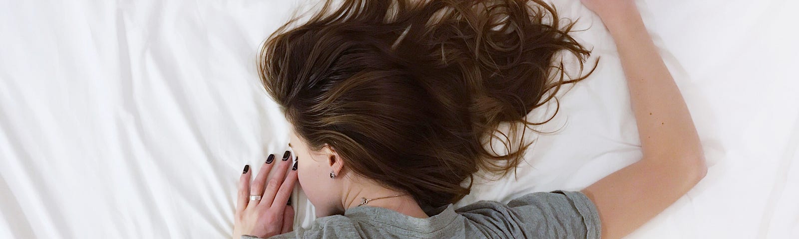 Young woman laying face down on bed sheets sleeping.