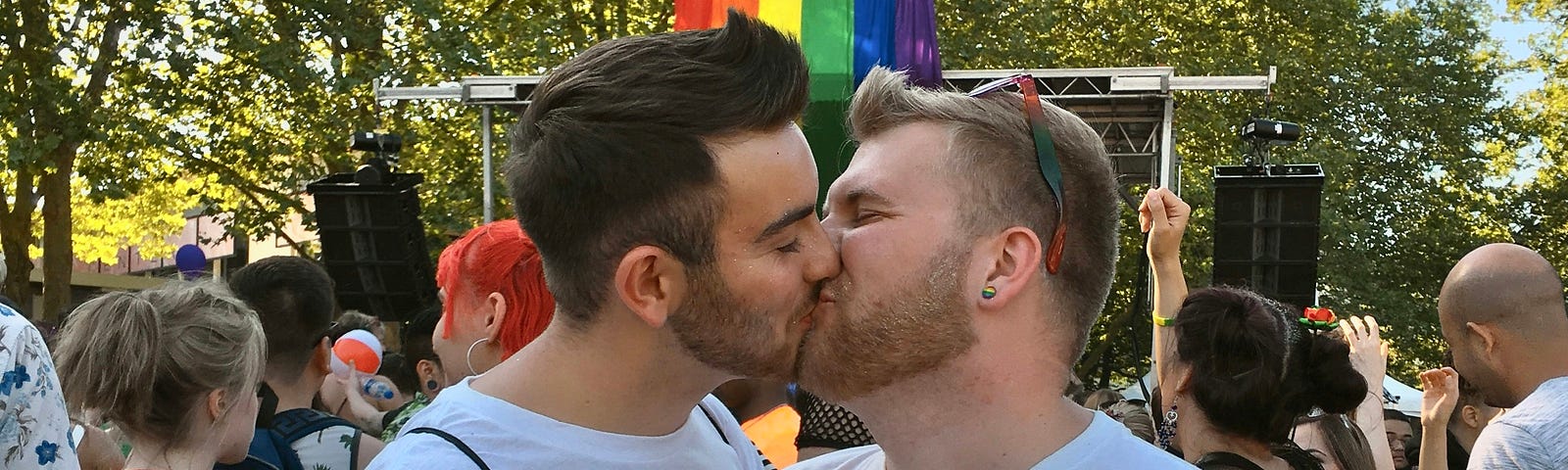 gay couple at pride kissing. Their t-shirts say “I am made in the image of God”