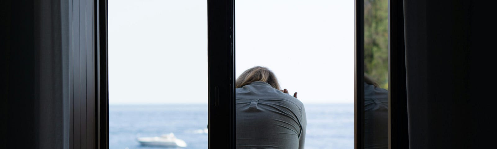 A woman standing on the balcony looks out at the ocean.