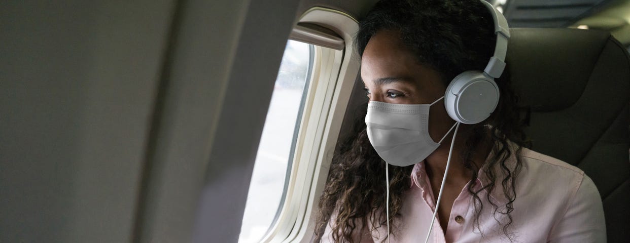 Masked passenger looking out plane window.