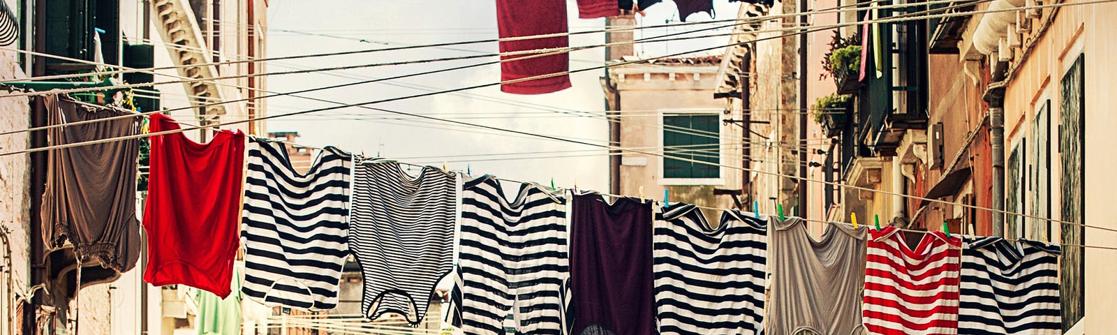 the space between two apartments with several laundry lines zigzagging. shirts are hanging on three of the lines against a pale blue sky