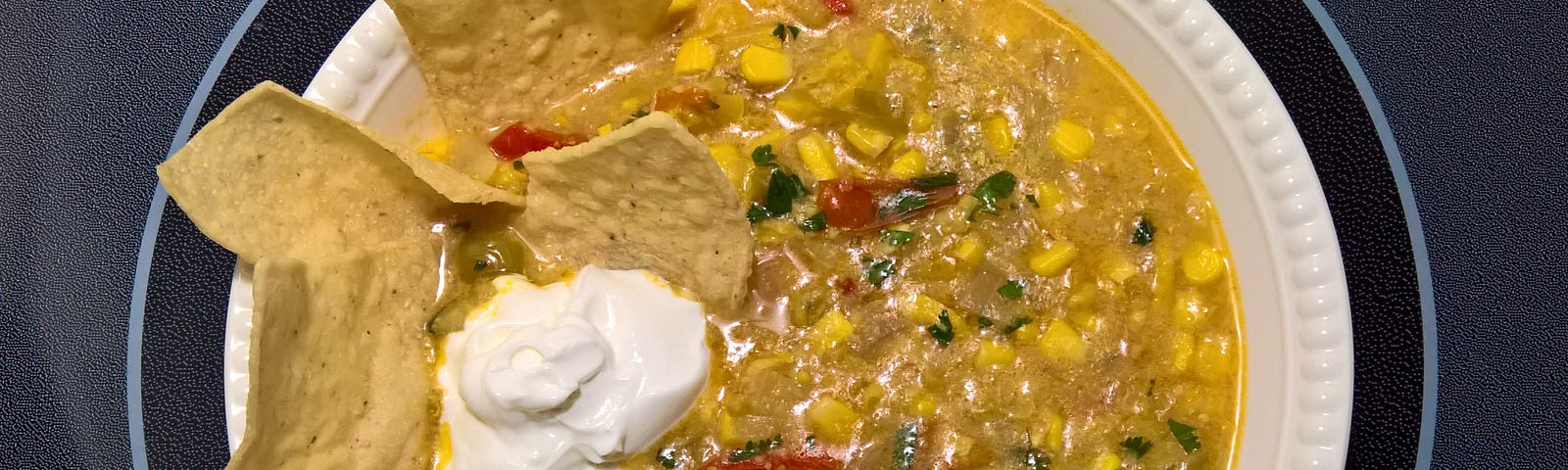 Corn, Squash, and Tomatillo Soup garnished with tortilla chips and sour cream.