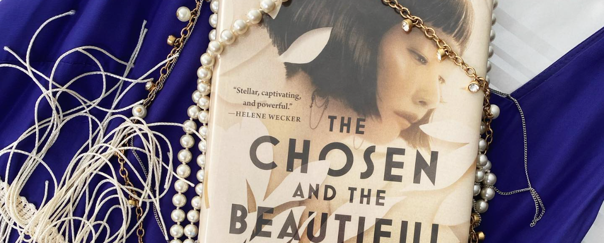 The Chosen and the Beautiful by Nghi Vo has the profile of an Asian woman on the cover with a bobbed, flapper haircut. Her expression is wistful and she’s surrounded by white flowers, as if they were cut out of paper. There are pearls and delicate gold necklaces draped over the book, which is laying on a white-fringed, purple flapper dress.