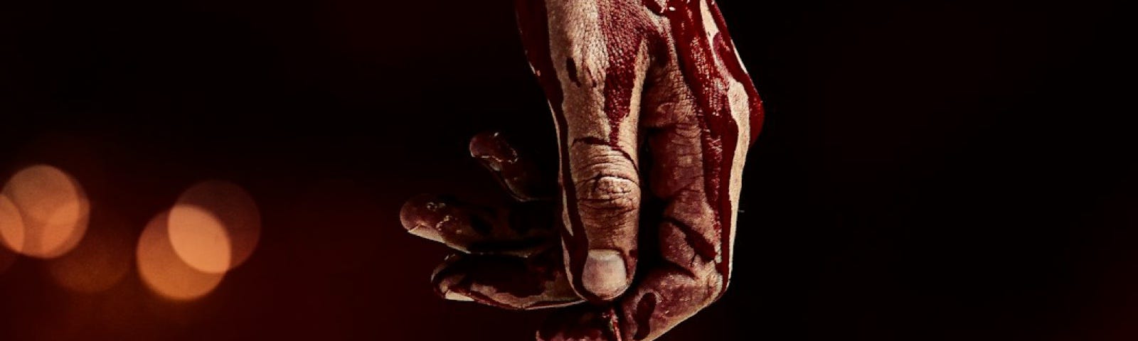 Against a black background, a bloodied hand reaches down, holding what looks like a heart wrapped in wire.