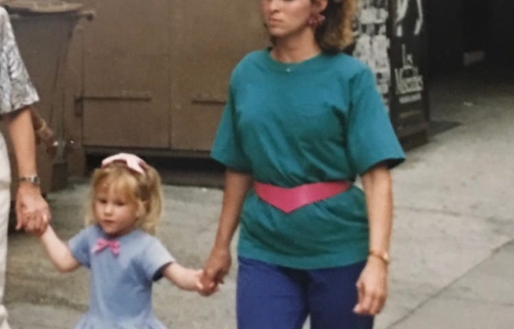 Photo of author and her 3 year old daughter. I’m wearing 80’s fashion from head to toe including purple leggings, a green teen shirt with shoulder pads, of course, Reebok sneakers and slouchy white socks.