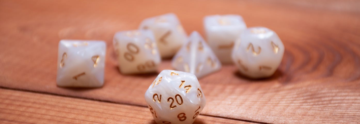 Image: A white dice set with gold numbering on a redwood tabletop.