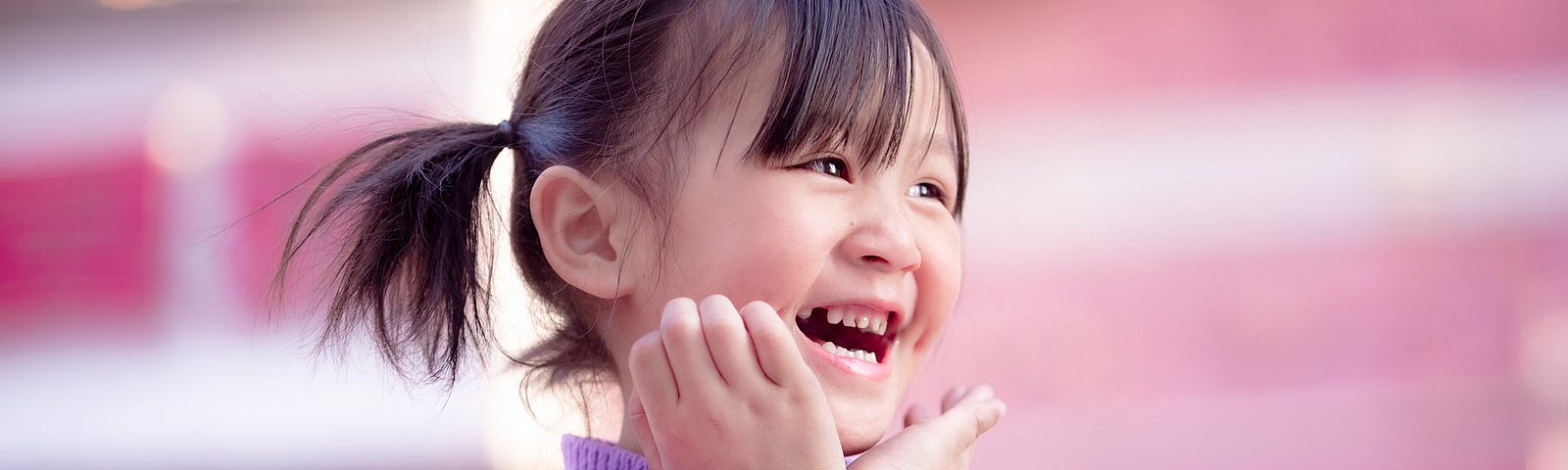 A young Asian girl with the widest smile is wearing a lavender sweater.