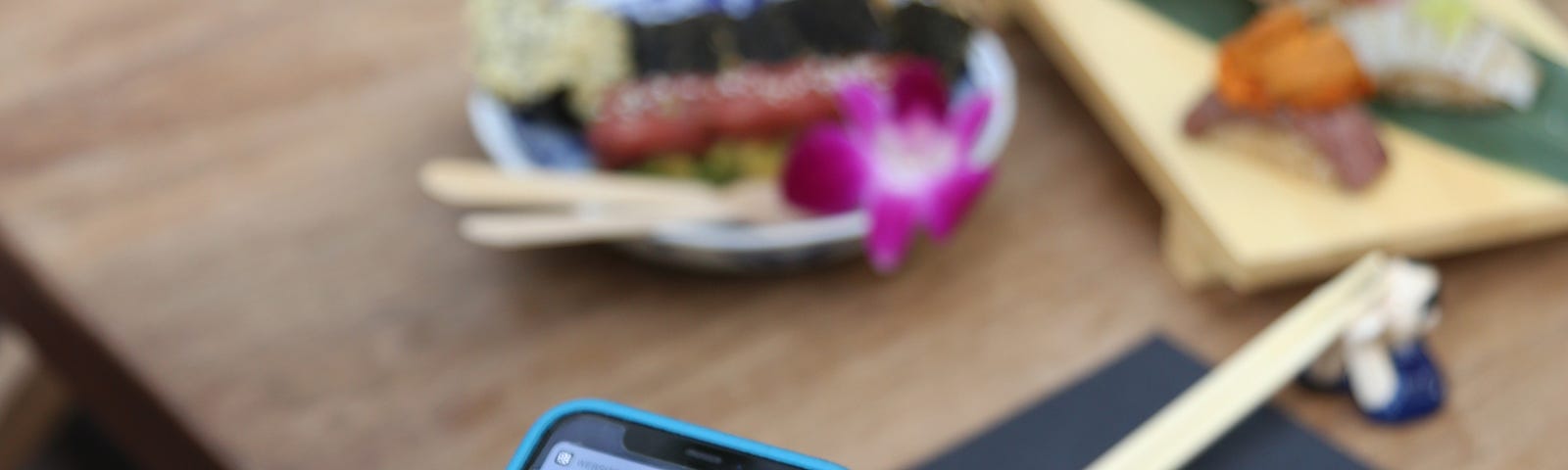 A phone scanning a QR code from a table that is laid with sushi plates.