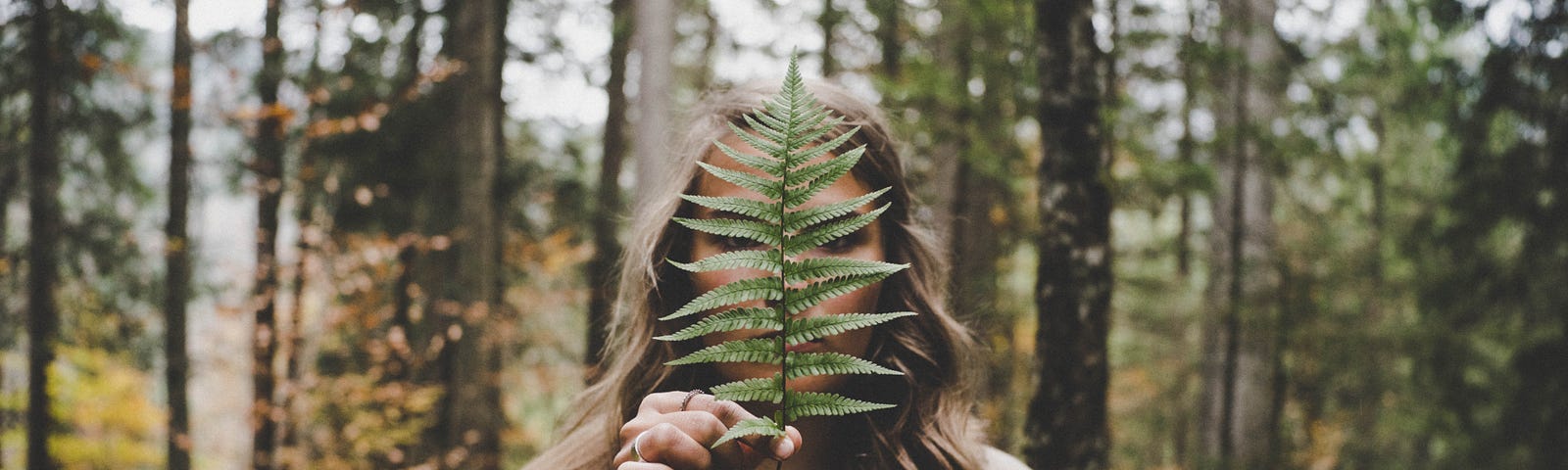 Woman standing in the woods holding a fern leave in front of their face