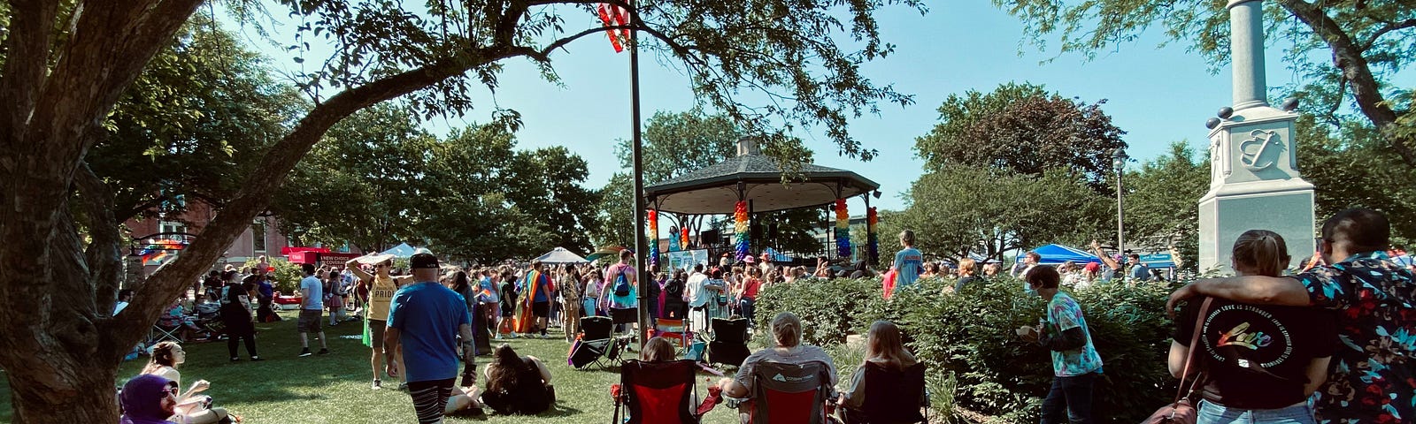 Large numbers of people at Pride in Woodstock, IL. Lots of rainbow flags.