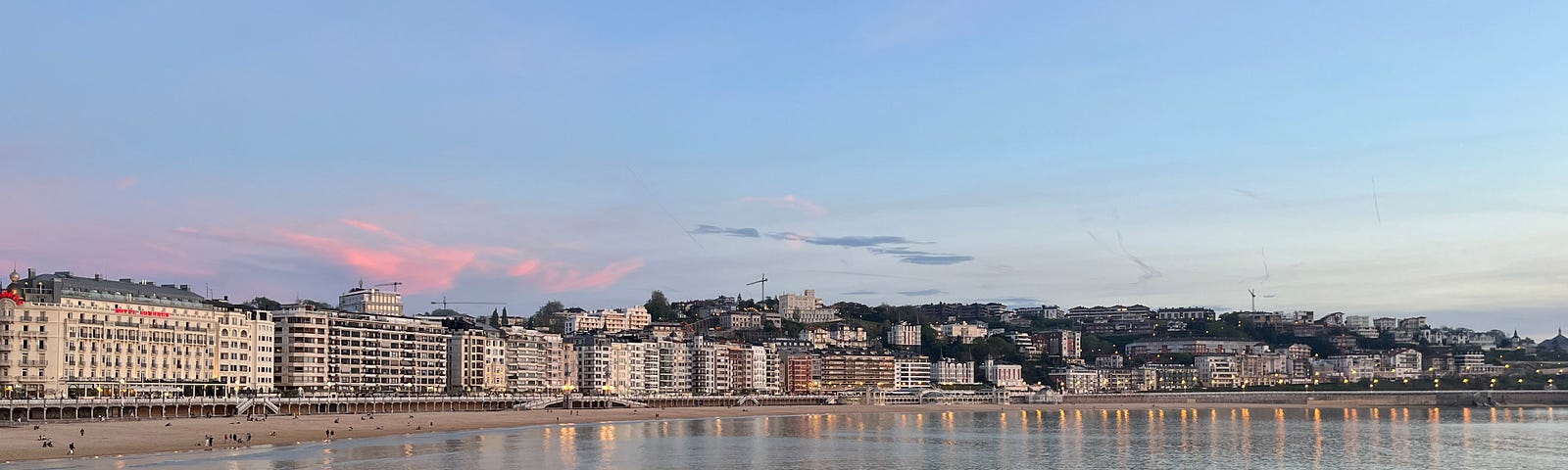 Sunset glows on the water and fronts of buildings that circle the beach in San Sebastian.