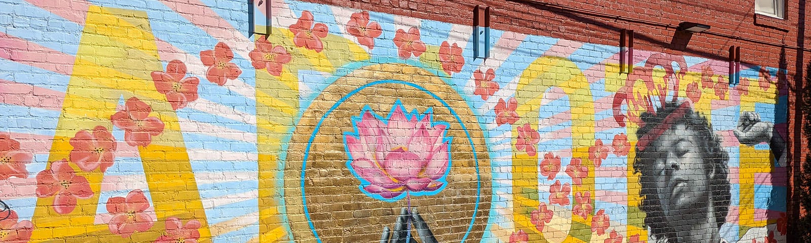 A colorful mural on a brick wall with large yellow letters in the background, a pink flower in the center, and Harry Styles on the right